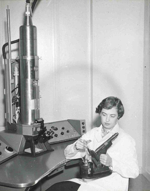 Dr. Elizabeth Hay, seated at the electron microscope, examines the first classroom microscope in America, devised by Oliver W. Holmes for demonstrations in histology in 1847.